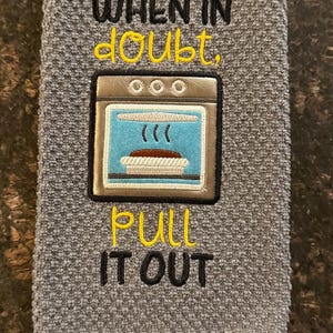 May include: Gray kitchen towel with embroidered text "WHEN IN DOUBT, PULL IT OUT" and an oven graphic. The oven graphic has a blue interior and a pie inside. The towel is made of a textured fabric.