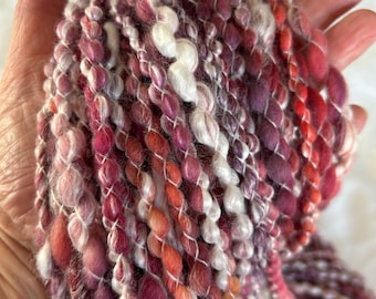 Puede incluir: Una madeja de hilo teñido a mano en tonos de rosa, rojo y blanco. El hilo está hecho de una mezcla de fibras, incluyendo lana y seda. El hilo es suave y esponjoso, y sería perfecto para tejer o hacer crochet una bufanda, gorro o manta.