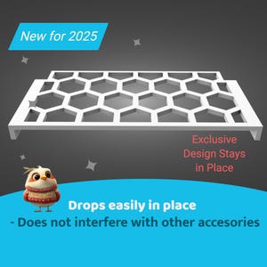 May include: White plastic shelf insert with a honeycomb design. The text "New for 2025" is in the top left corner. The text "Exclusive Design Stays in Place" is in the bottom right corner. The text "Drops easily in place - Does not interfere with other accessories" is in the bottom center.