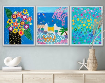 May include: Three framed paintings with colorful floral and landscape designs. The paintings are hung on a light blue wall above a wooden shelf.