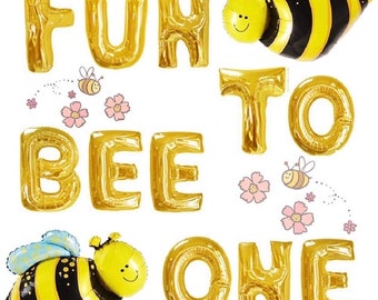 May include: Gold foil letter balloons spelling "Fun to Bee One" with two cartoon bee balloons. The bees are yellow and black with black eyes and smiles.
