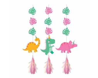 May include: Three dinosaur party hanging decorations with green leaves and pink tassels. The dinosaurs are a green T-Rex, a yellow brachiosaurus, and a pink triceratops.