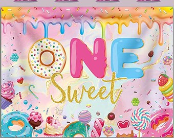 May include: A pink and blue backdrop with the word "ONE" in pink and blue letters with a donut and sprinkles. The text "Sweet" is in gold glitter letters. The backdrop is perfect for a first birthday party.
