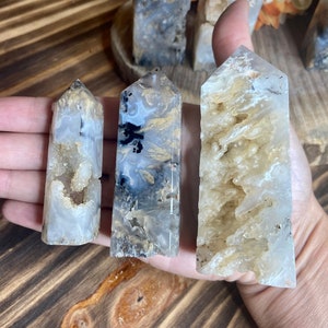 May include: Three agate crystal points with different patterns and colors. The points are white, gray, and brown with black and white swirls. The points are arranged in a row on a hand.