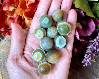 May include: A collection of green, brown, and white agate spheres. The spheres are smooth and polished, with intricate patterns of color.