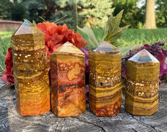 Puede incluir: Cuatro torres de piedras preciosas pulidas, multicolores, con bandas y facetadas. Las torres están dispuestas en fila sobre una superficie de madera. Las torres son una mezcla de marrón, naranja, amarillo y blanco.
