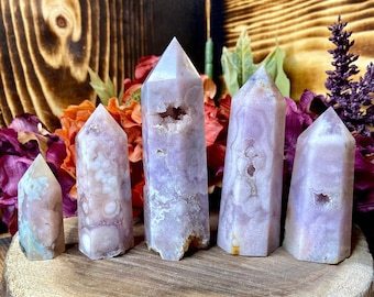 May include: Five amethyst crystal points of varying sizes, arranged on a wooden slice. The points are a pale lavender colour with white and grey inclusions.