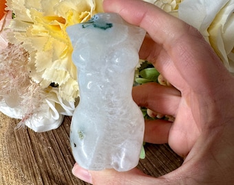 May include: White crystal sculpture of a female torso with green inclusions. The sculpture is smooth and polished.