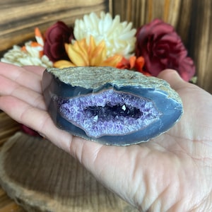 May include: A purple amethyst geode with a natural crystal formation. The geode is partially open, revealing the amethyst crystals inside. The geode is a natural stone and has a rough, textured surface.