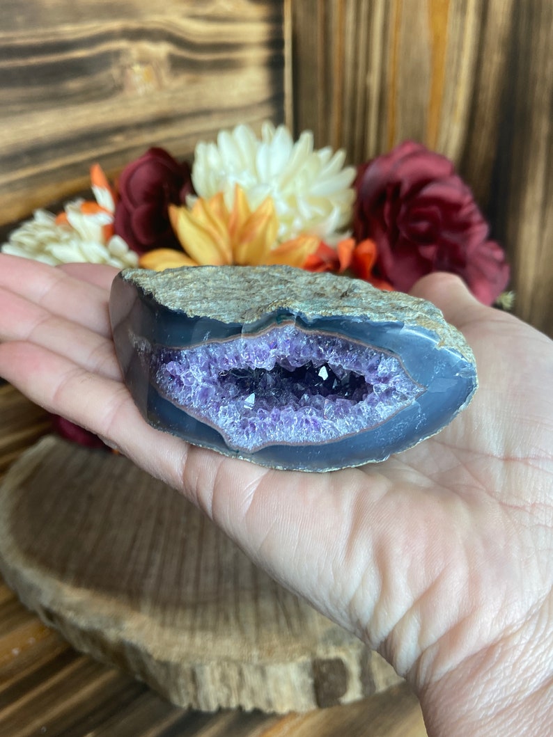 May include: A purple amethyst geode with a natural crystal formation. The geode is partially open, revealing the amethyst crystals inside. The geode is a natural stone and has a rough, textured surface.