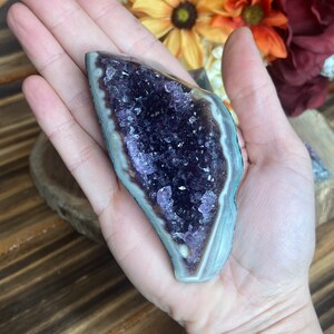 May include: A purple amethyst crystal cluster with a natural, raw edge and a smooth, polished exterior. The crystal is a deep purple colour and has a natural, white, banded pattern.