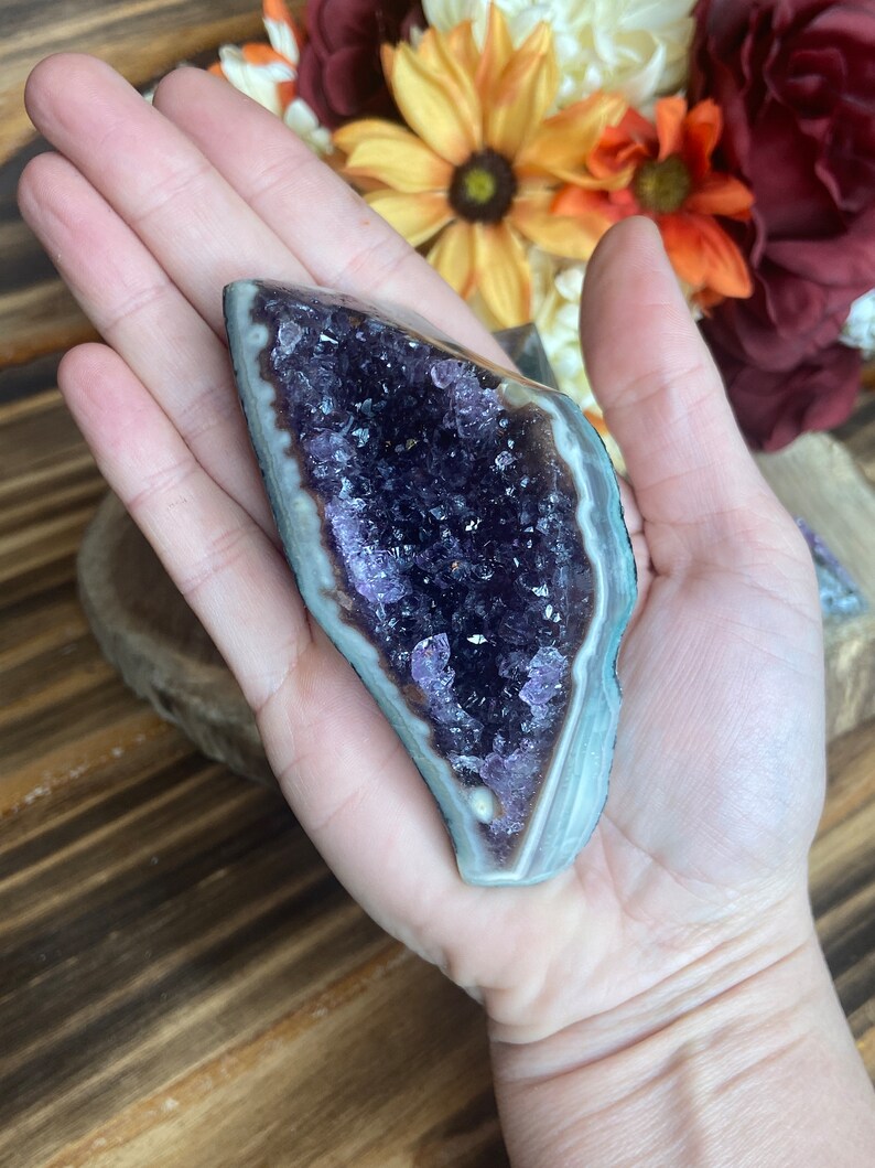 May include: A purple amethyst crystal cluster with a natural, raw edge and a smooth, polished exterior. The crystal is a deep purple colour and has a natural, white, banded pattern.