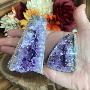 May include: Two amethyst crystal geodes with a purple and white colour scheme. The geodes are in the shape of a triangle and have a natural, rough texture.