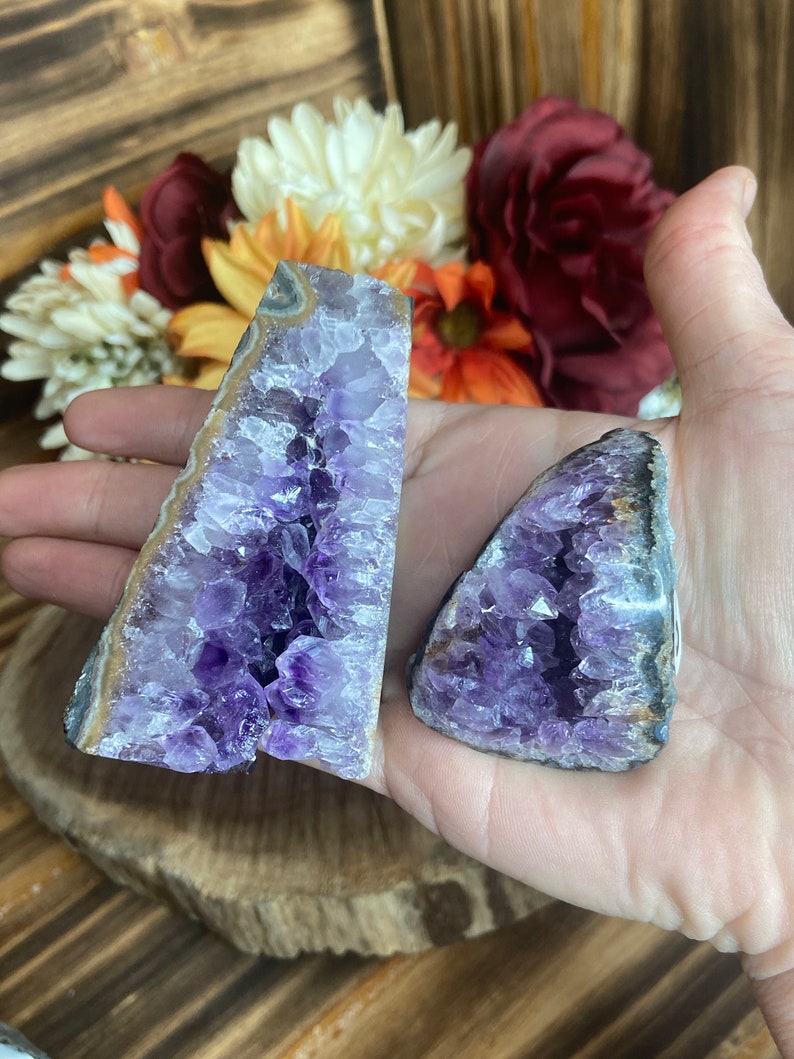 May include: Two amethyst crystal geodes with a purple and white colour scheme. The geodes are in the shape of a triangle and have a natural, rough texture.