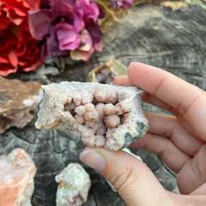 May include: A pink and white crystal cluster with a natural, rough exterior. The crystal has a hollow center filled with smaller crystals.