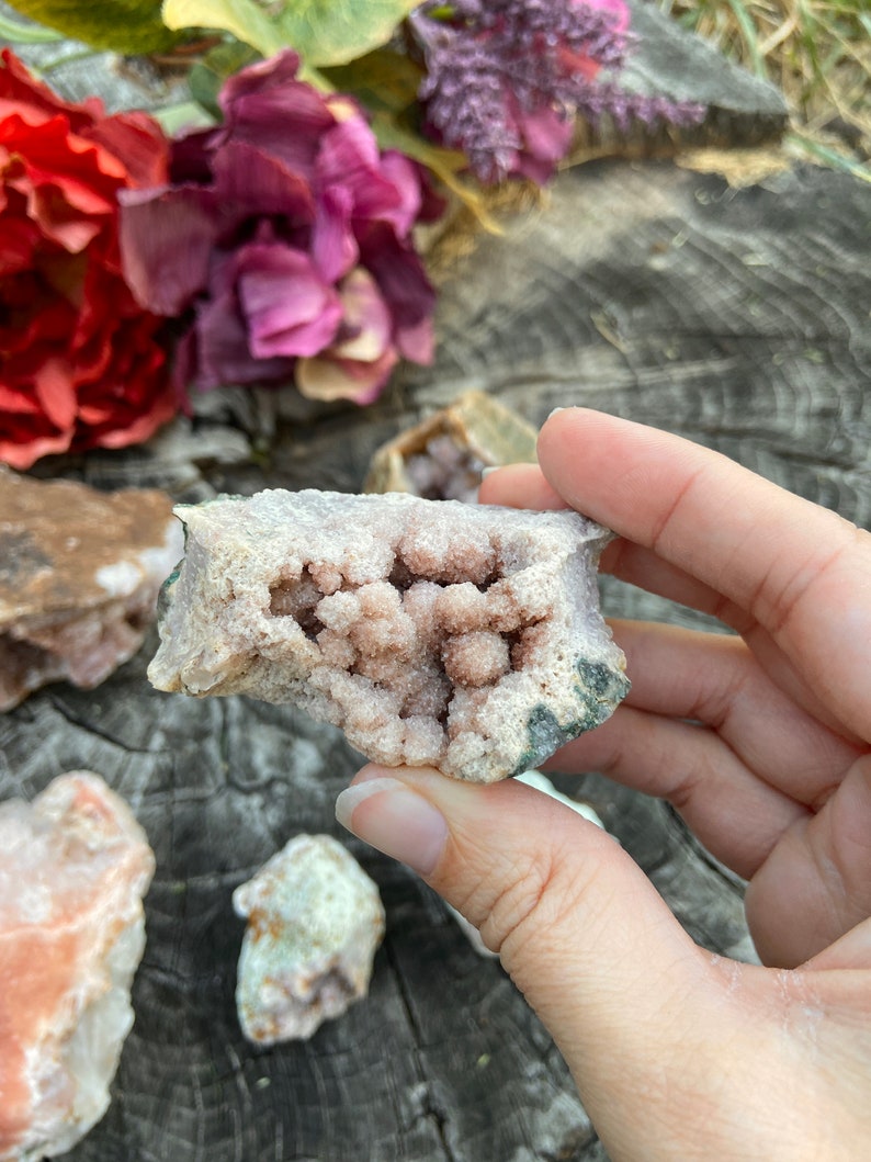 May include: A pink and white crystal cluster with a natural, rough exterior. The crystal has a hollow center filled with smaller crystals.
