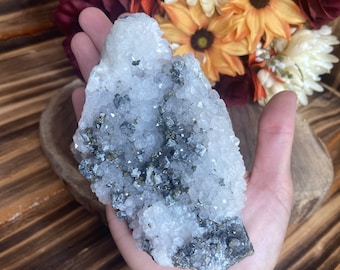 Può includere: Un ammasso di cristalli bianco e grigio con una texture ruvida e naturale. Il cristallo è una combinazione di quarzo trasparente e pirite grigia.