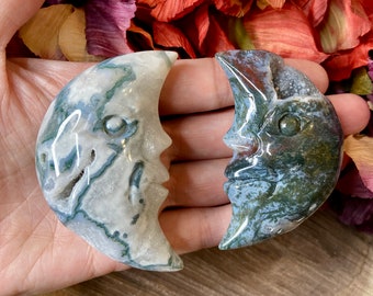 May include: Two green, white, and gray agate crescent moon carvings with faces. The carvings are smooth and polished.