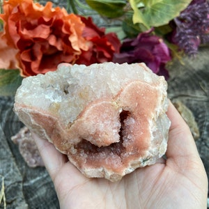 May include: A pink and white crystal cluster with a large, open cavity. The crystal is rough and has a natural, organic shape.