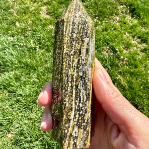 May include: A green and brown crystal point with white flecks. The crystal is pointed at the top and has a flat base.
