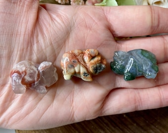 May include: Three small carved animal figurines made of agate. The figurines are a turtle, a pig, and a frog. The turtle is green, the pig is brown and white, and the frog is pink and white.