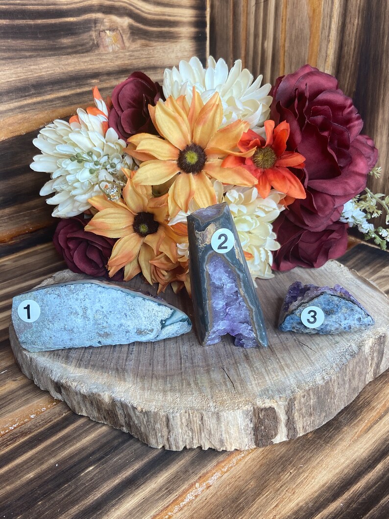 May include: Three amethyst geodes, one with a purple interior, one with a grey interior, and one with a blue interior, on a wooden slice. The geodes are numbered 1, 2, and 3.