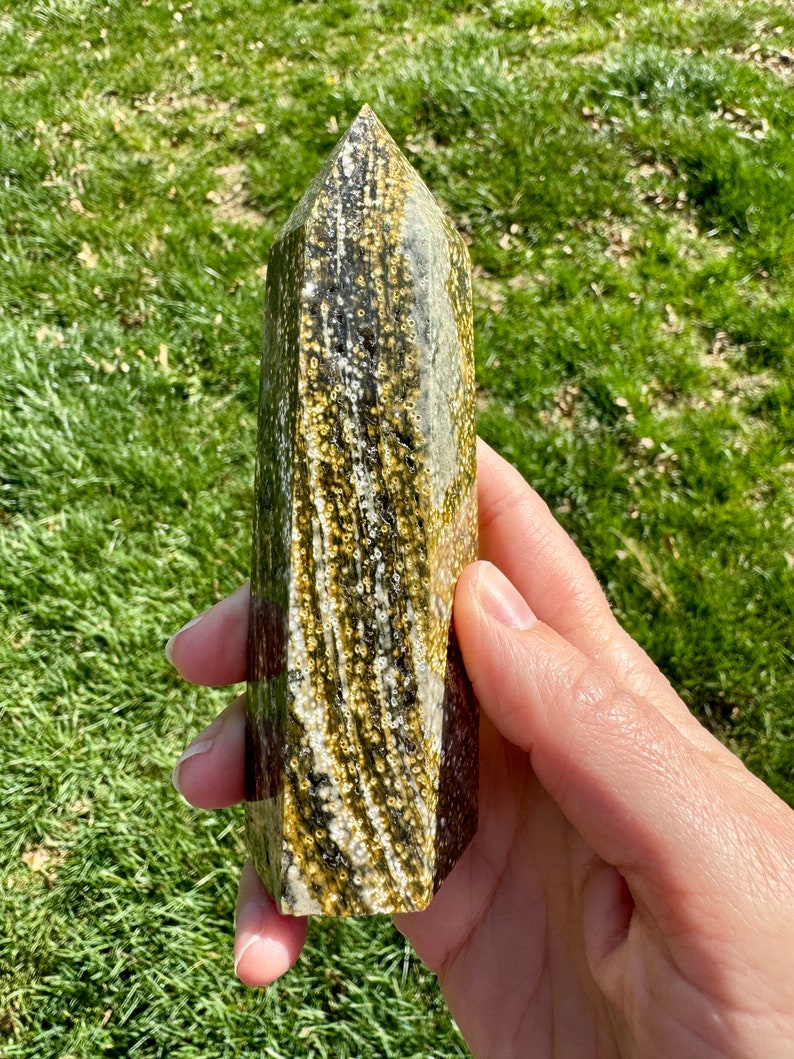 May include: A green and gold crystal point with a unique, swirling pattern. The crystal is polished and has a smooth, glassy finish.