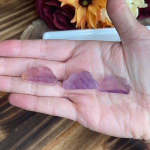 May include: Three purple and pink cloud-shaped crystal stones. The stones are smooth and polished.
