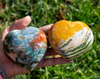 May include: Two heart-shaped polished stones, one with a green, blue, and orange pattern, and the other with a yellow, white, and green pattern.