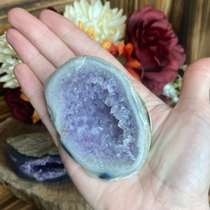 May include: A purple amethyst geode with a natural crystal formation. The geode is partially open, revealing the purple crystals inside. The geode is a light grey colour on the outside.