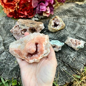 May include: A cluster of pink and white crystals with a large, open cavity in the center. The crystals are arranged in a natural, organic pattern. The crystals are on a wooden surface.