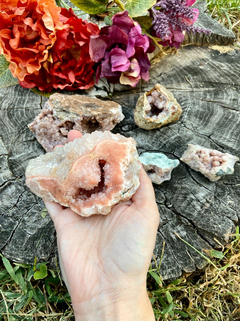 May include: A cluster of pink and white crystals with a large, open cavity in the center. The crystals are arranged in a natural, organic pattern. The crystals are on a wooden surface.