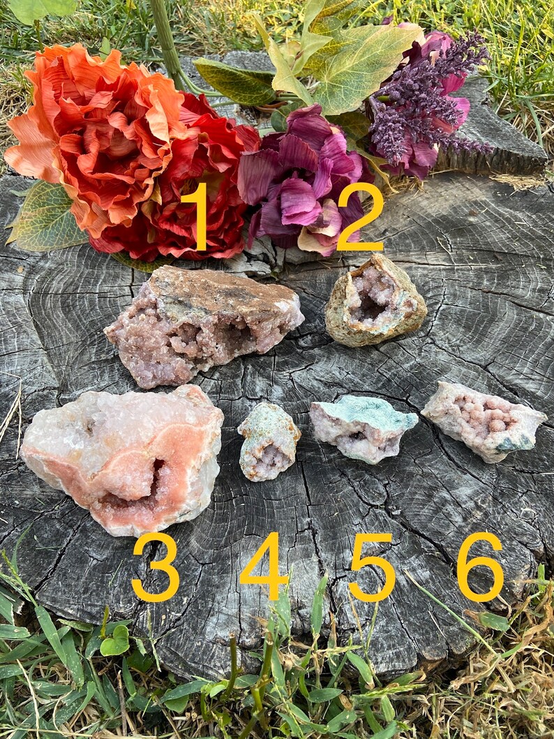 May include: Six pink and white crystal clusters with a variety of shapes and sizes. The crystals are arranged on a wooden surface with numbers 1 through 6 written on the surface.