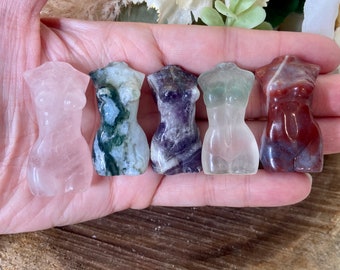 May include: Five small carved stone sculptures of female figures in various colours, including pink, green, purple, clear, and red.