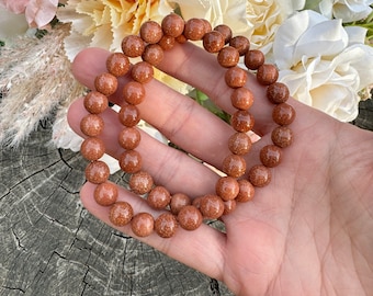 May include: A brown sandstone beaded bracelet with a natural, earthy look. The bracelet is made of round beads and is strung on a stretchy cord.