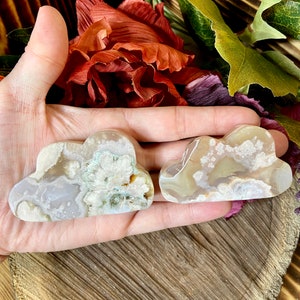 May include: Two white agate cloud shaped stones with brown and green inclusions. The stones are smooth and polished.