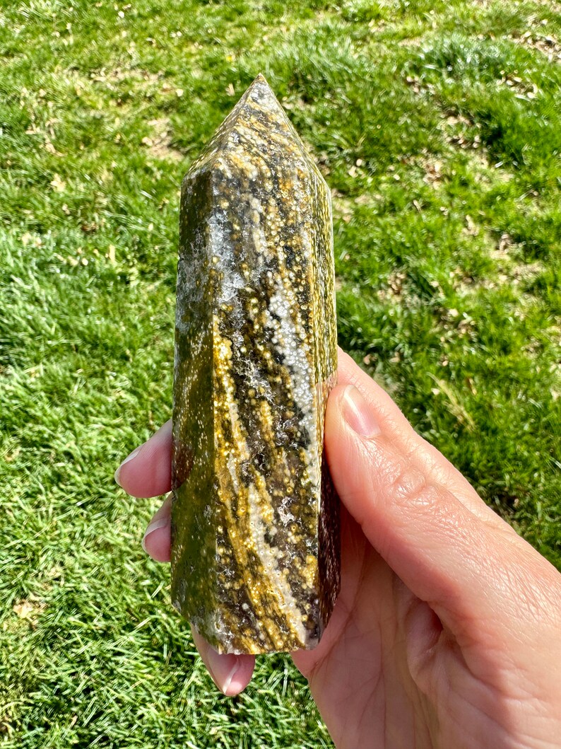 May include: A green and gold crystal point with a unique swirling pattern. The crystal is polished and has a smooth, glassy finish.