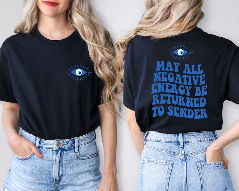 Puede incluir: Camiseta negra con un dise&ntilde;o de ojo azul en la parte delantera y trasera. La parte trasera de la camiseta presenta el texto "MAY ALL NEGATIVE ENERGY BE RETURNED TO SENDER" en azul. La camiseta es de material suave.