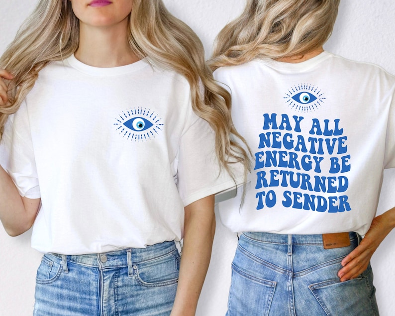Puede incluir: Camiseta blanca con un gr&aacute;fico de ojo azul en la parte delantera y el texto "MAY ALL NEGATIVE ENERGY BE RETURNED TO SENDER" en la parte trasera. El gr&aacute;fico del ojo es un dise&ntilde;o estilizado con un iris azul y l&iacute;neas radiantes.