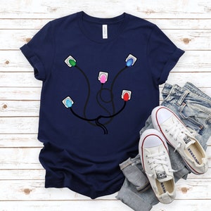 May include: A navy blue t-shirt with a graphic of a heart monitor with four colored leads. The leads are green, pink, blue, and red.