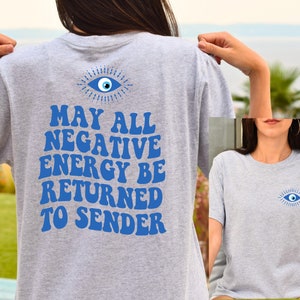 Puede incluir: Camiseta gris claro con un dise&ntilde;o de ojo azul en la parte delantera y trasera. La parte trasera de la camiseta presenta el texto "MAY ALL NEGATIVE ENERGY BE RETURNED TO SENDER" en azul, con letras de estilo retro.