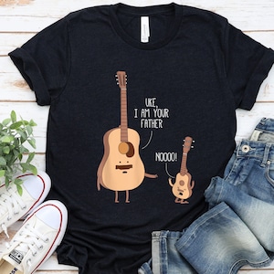 May include: A black t-shirt with a funny illustration of two guitars. The larger guitar says "Uke, I am your father" and the smaller guitar says "Noooo!"