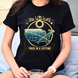May include: Black t-shirt with a graphic of a total solar eclipse over a map of the United States. The graphic includes the years 2017 and 2024 and the text "Total Solar Eclipse" and "Twice in a Lifetime".