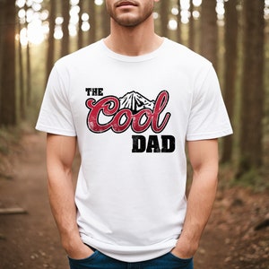 May include: White t-shirt with a red graphic that says "The Cool Dad" with a mountain design.