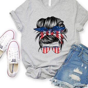 May include: A grey t-shirt featuring a graphic of a woman's hair in a messy bun with a red, white and blue bandana. The bandana has a splatter paint design. The woman is wearing sunglasses with a red, white and blue striped design.