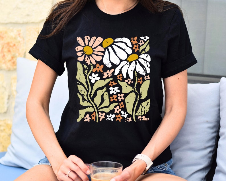 May include: A black t-shirt with a floral print featuring white, pink, and yellow daisies with green leaves and stems. The print has a distressed, vintage look.