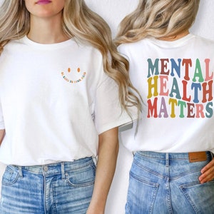 May include: White t-shirt with the text "Be Kind to Your Mind" in rainbow colors and a smiley face on the front. The back of the shirt has the text "Mental Health Matters" in rainbow colors.