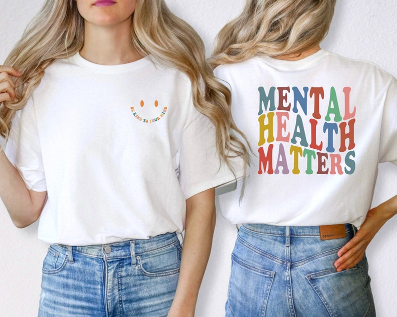 May include: White t-shirt with the text "Be Kind to Your Mind" in rainbow colors and a smiley face on the front. The back of the shirt has the text "Mental Health Matters" in rainbow colors.