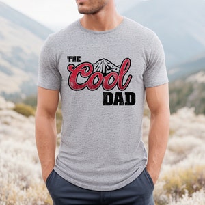 May include: A gray t-shirt with a red and black graphic that says "The Cool Dad" with a mountain silhouette.