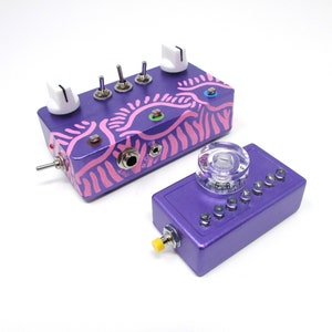 Puede incluir: Pedal de música electrónica morado y rosa con botones, interruptores y un dial de plástico transparente. El pedal tiene un diseño a rayas rosa y blanco con un patrón de ondas rosa y blanco.